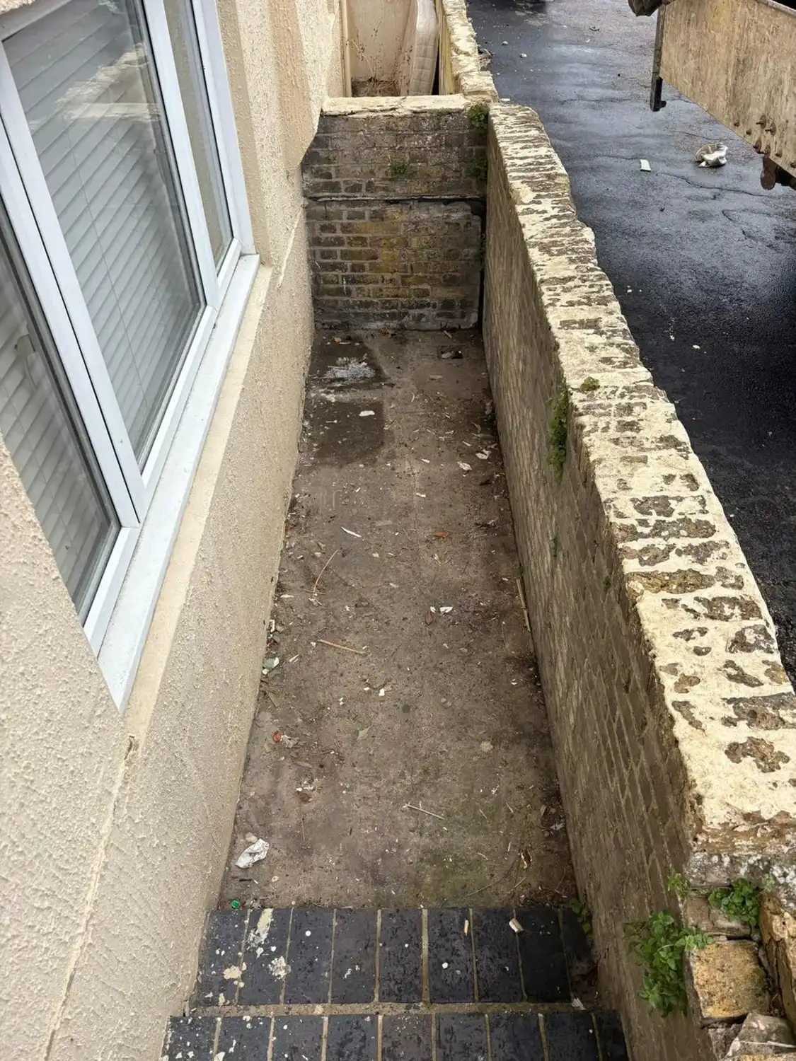 An alley way with a brick wall next to a window.