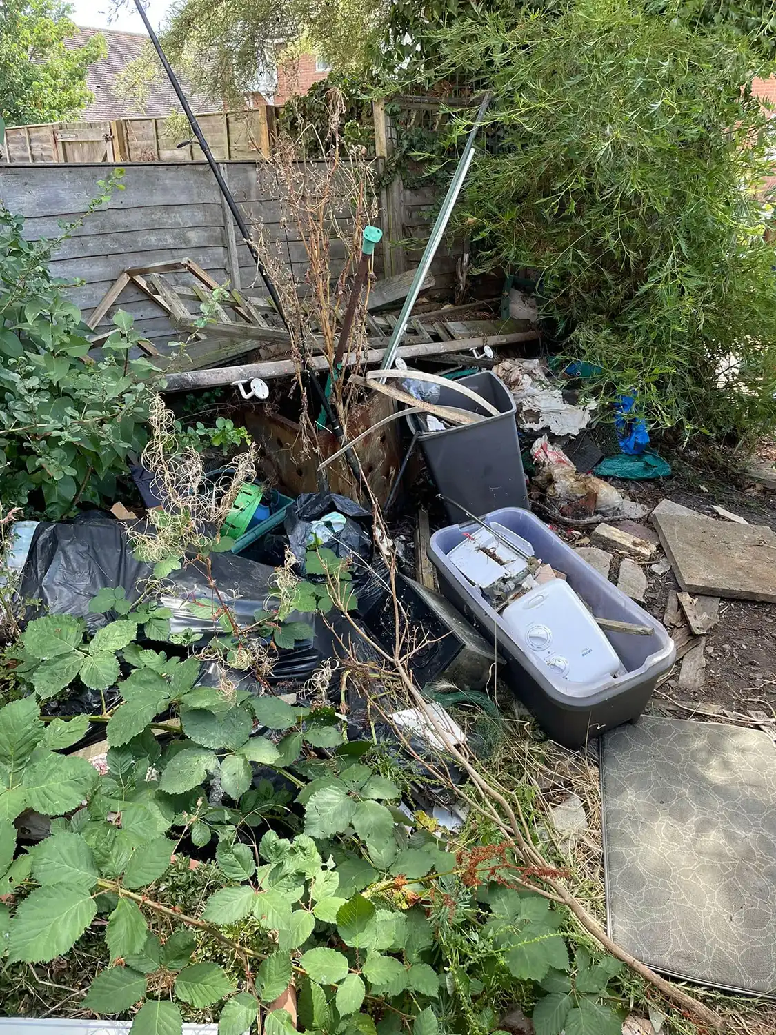A pile of trash sitting in a garden next to a fence.